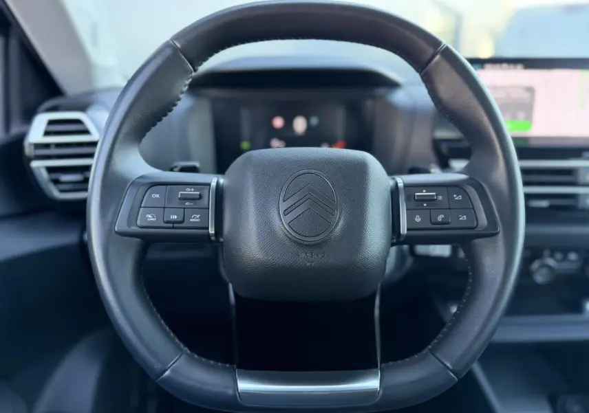 Vue rapprochée du volant en cuir noir de la Citroën C4 Hybrid 145, avec commandes intégrées et tableau de bord flou.