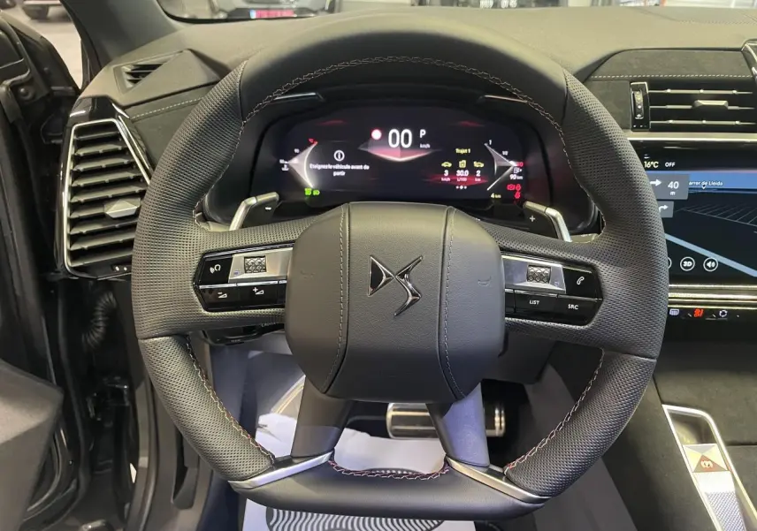 Vue rapprochée du volant en cuir perforé noir avec surpiqûres Carmin et Or du DS7 Crossback gris titanium, tableau de bord numérique visible.