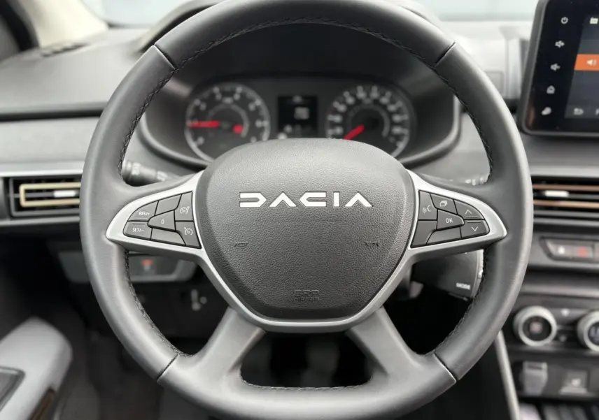 Gros plan sur le volant noir du Dacia Jogger 2025 avec commandes intégrées et tableau de bord flou en arrière-plan.