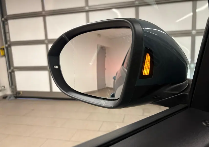 Rétroviseur extérieur droit du Volkswagen T-Roc bleu pétrole 2025 avec clignotant orange allumé en intérieur.