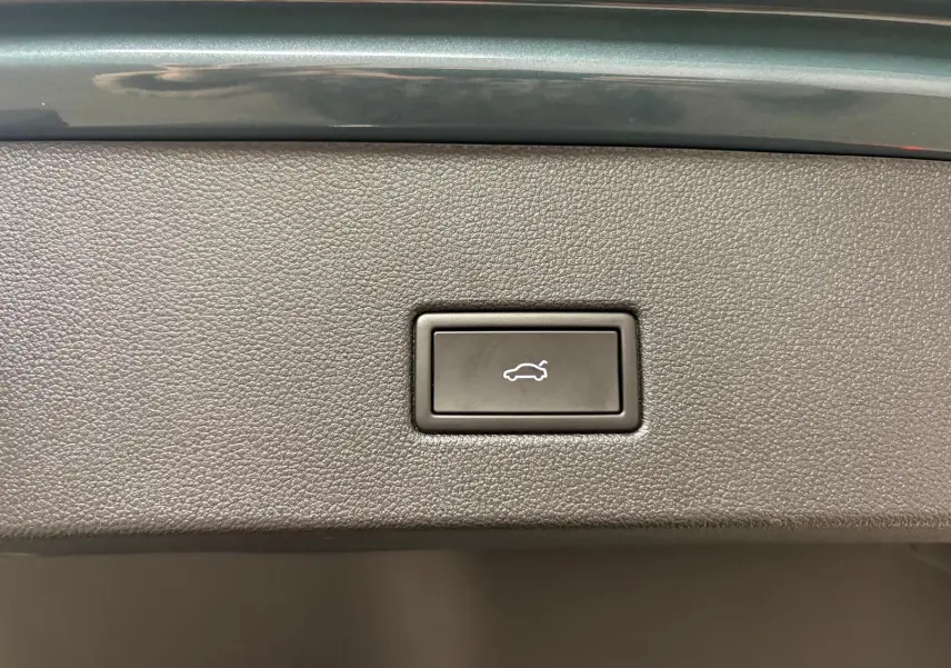 Bouton d'ouverture électrique du coffre sur panneau intérieur avec finition noire texturée, détail du Volkswagen T-Roc bleu pétrole 2025.