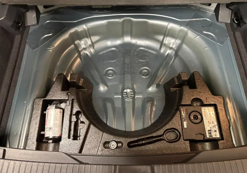 Coffre ouvert montrant le rangement sous plancher avec kit de réparation et espace pour roue de secours du Volkswagen T-Roc 2025.