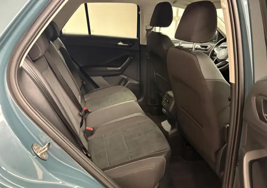 Vue intérieure arrière droite du Volkswagen T-Roc bleu pétrole 2025, montrant les sièges arrière en tissu noir avec surpiqûres blanches.