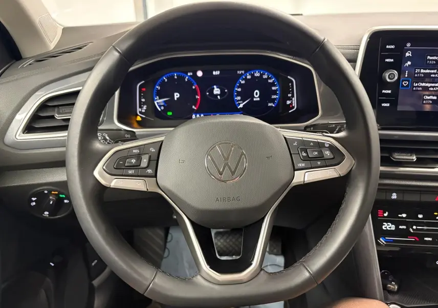 Vue centrée sur le volant multifonction noir du Volkswagen T-Roc 2025, avec tableau de bord digital et commandes visibles.