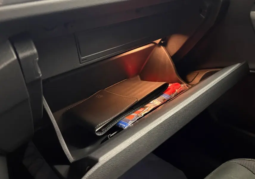 Boîte à gants ouverte du Volkswagen T-Roc bleu pétrole 2025, montrant un étui en cuir noir à l'intérieur.