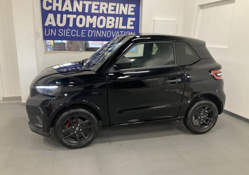 Vue de profil côté gauche d'une LIGIER JS50 0.5 REVO D+ SELECT noire avec jantes alu noires et feux LED en intérieur showroom.