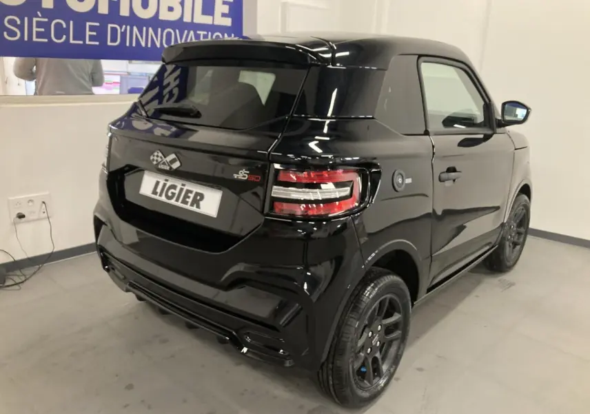 Vue 3/4 arrière droite d'une Ligier JS50 noire 2026 avec jantes alu noires et feux LED distinctifs en intérieur showroom.