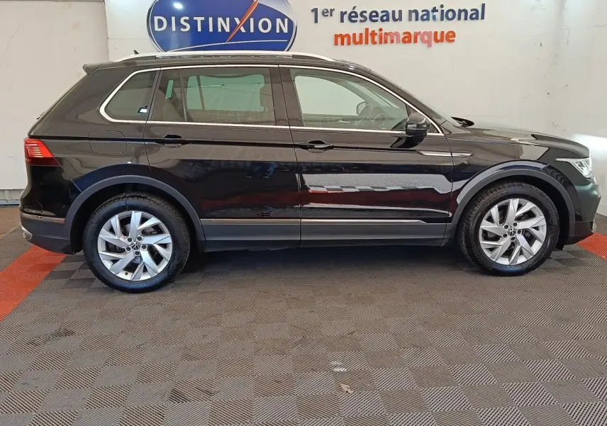 Vue latérale droite d'un Volkswagen Tiguan noir 2022 avec jantes alliage et rails de toit chromés en intérieur showroom.