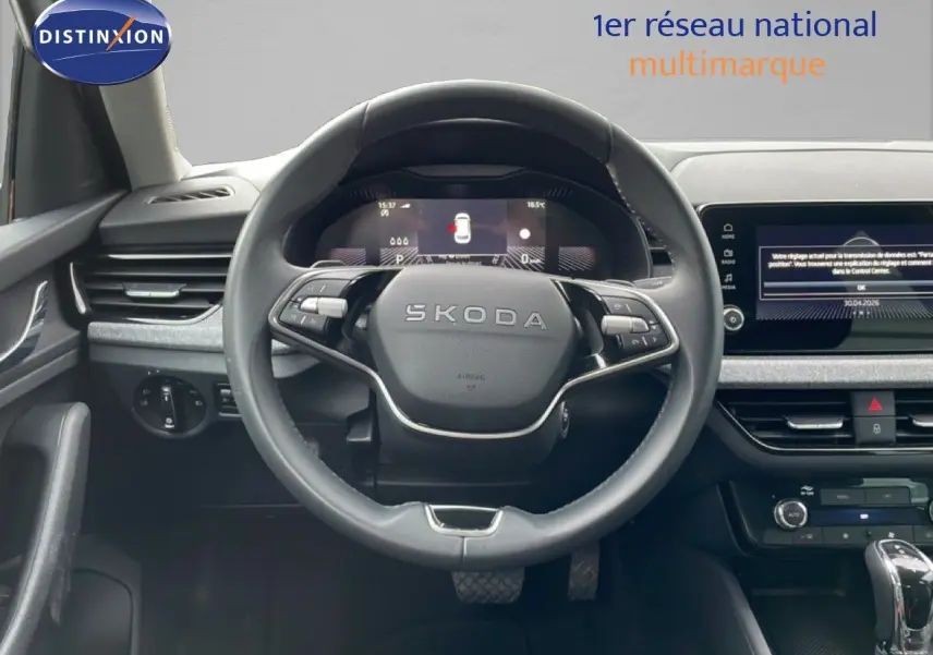 Vue intérieure centrée sur le volant SKODA d’un KAMIQ blanc glacier 2025 avec tableau de bord numérique et écran tactile.