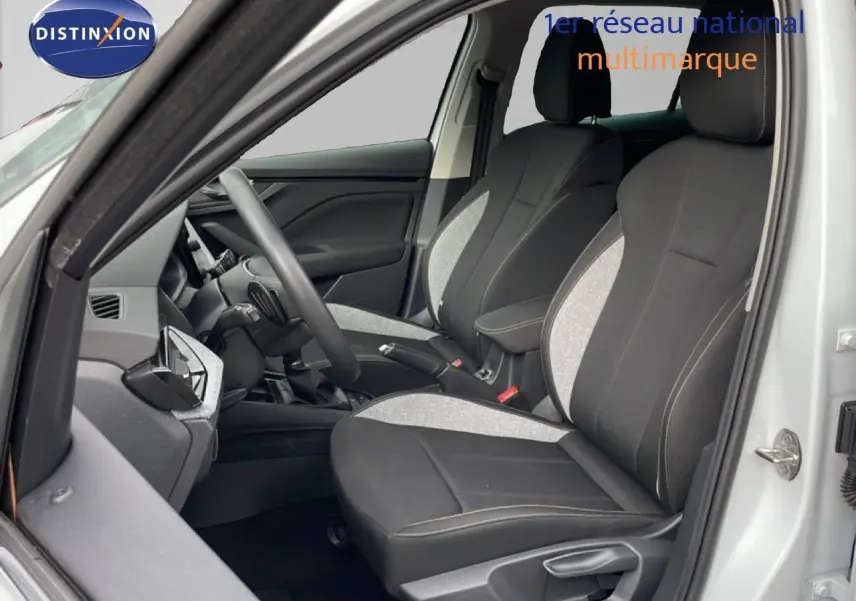 Vue intérieure côté conducteur du Skoda Kamiq blanc glacier 2025, sièges tissu bicolore gris et noir avec volant multifonctions.