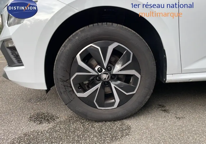 Gros plan sur la roue avant gauche du Skoda Kamiq blanc glacier, mettant en valeur la jante noire et argentée au design moderne.