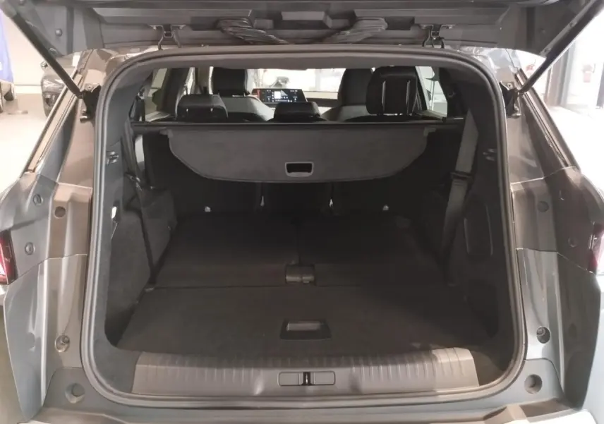 Coffre ouvert vu de l'arrière d'un Peugeot 5008 gris titanium avec banquette arrière rabattue et cache-bagages déployé.