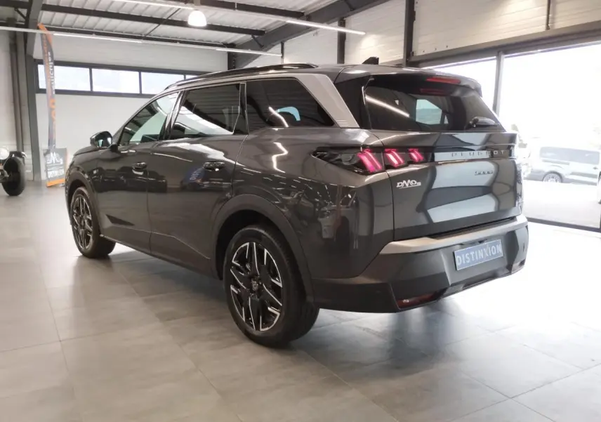 Peugeot 5008 gris titanium vue 3/4 arrière droit en intérieur avec feux arrière LED 3 griffes allumés.