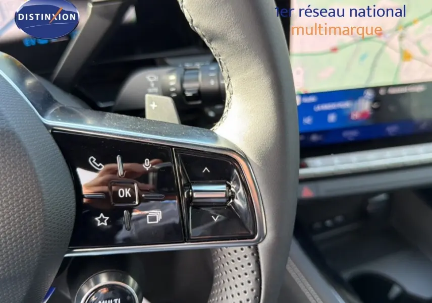 Gros plan sur les commandes gauche du volant du Renault Espace noir étoile métal, avec écran tactile flou en arrière-plan.