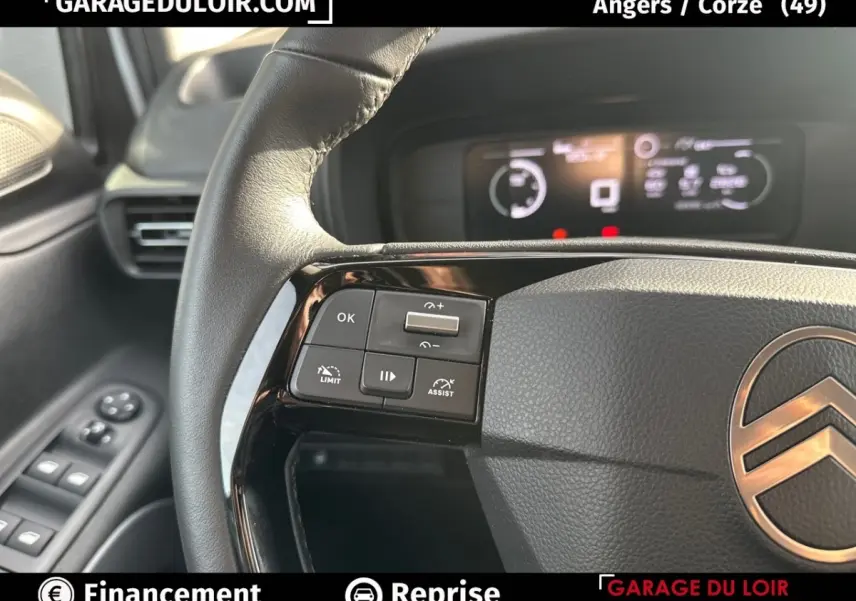 Gros plan sur le volant cuir multifonctions côté gauche du Citroën Berlingo gris clair avec tableau de bord numérique flou.