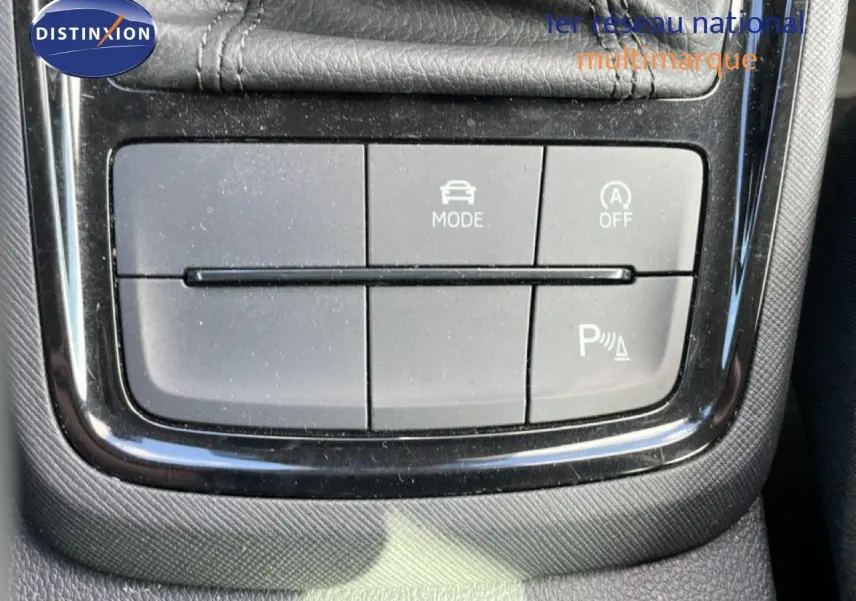 Gros plan sur les boutons de commande du mode de conduite et assistance au stationnement dans la console centrale d’un Skoda Kamiq gris argent.