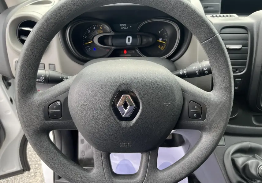 Vue rapprochée du volant noir et du tableau de bord du Renault Trafic Fourgon blanc, version 2016, avec commandes au volant visibles.