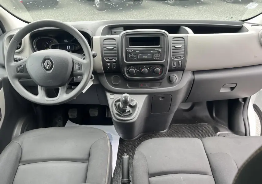 Intérieur avant du Renault Trafic Fourgon blanc 2016, tableau de bord gris clair et volant noir avec levier de vitesse manuel.