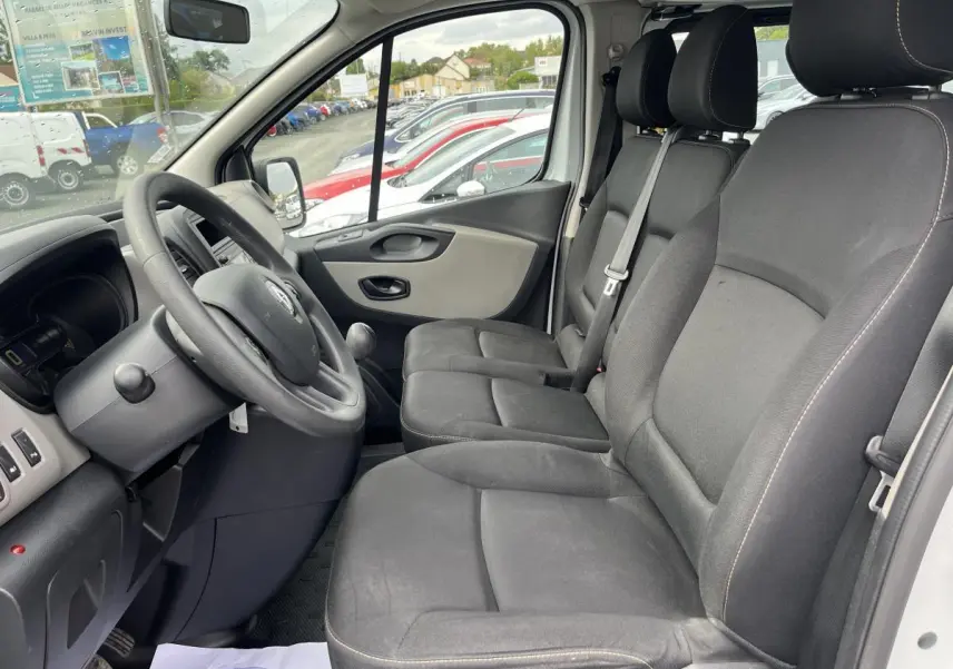 Intérieur avant du Renault Trafic Fourgon blanc 2016, sièges noirs avec ceintures de sécurité et volant visible côté conducteur.