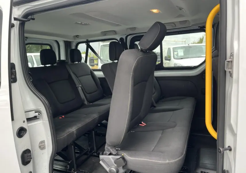 Intérieur du Renault Trafic blanc vu côté gauche, montrant les banquettes noires 3 rangées avec ceintures de sécurité.
