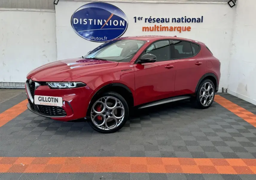 Vue 3/4 avant gauche d'un Alfa Romeo Tonale rouge avec jantes spécifiques et étriers de frein rouges sur fond intérieur showroom.