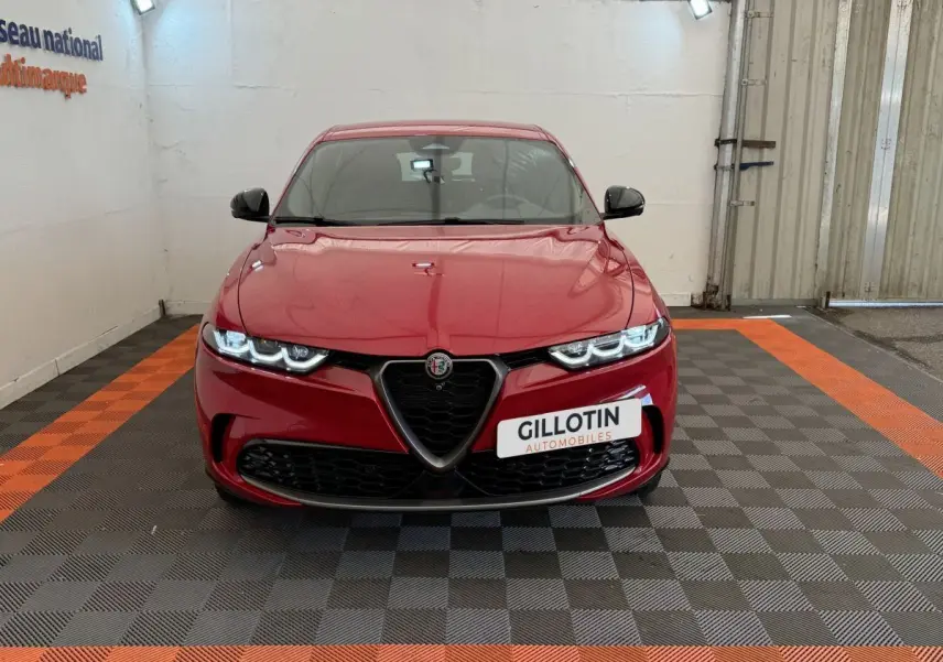 Vue de face de l'Alfa Romeo Tonale rouge 2023 avec calandre emblématique et phares LED allumés dans un showroom.