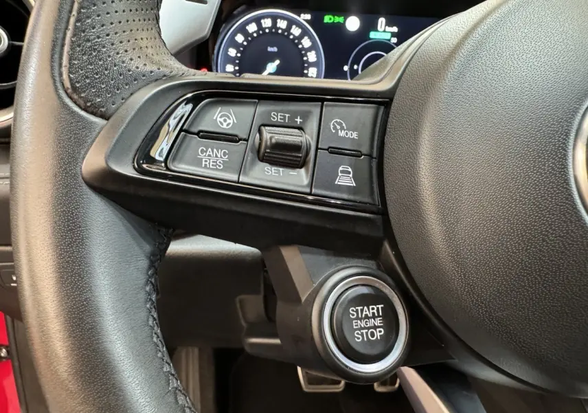 Gros plan sur le volant cuir noir de l'Alfa Romeo Tonale rouge, avec commandes de régulateur et bouton start/stop visible.