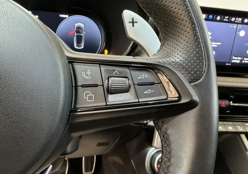 Gros plan sur les commandes du volant cuir perforé de l'Alfa Romeo Tonale rouge, avec écran digital en arrière-plan.