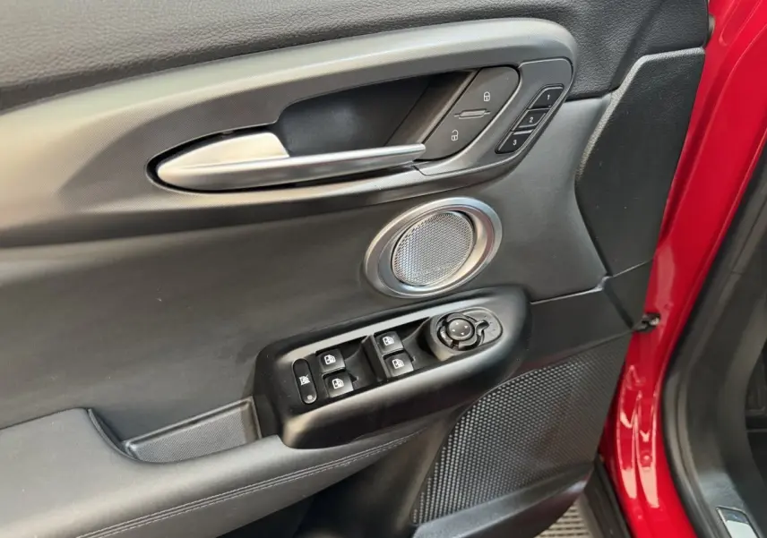 Gros plan sur la porte avant gauche rouge d'une Alfa Romeo Tonale, avec commandes de vitres et haut-parleur intégré.