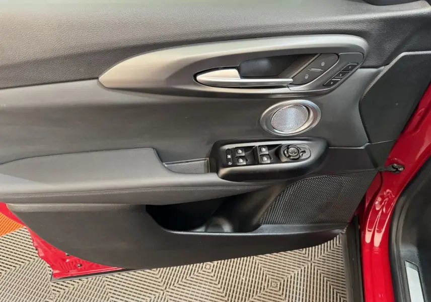 Gros plan sur la porte avant gauche rouge de l'Alfa Romeo Tonale avec commandes de vitres et haut-parleur intégré.