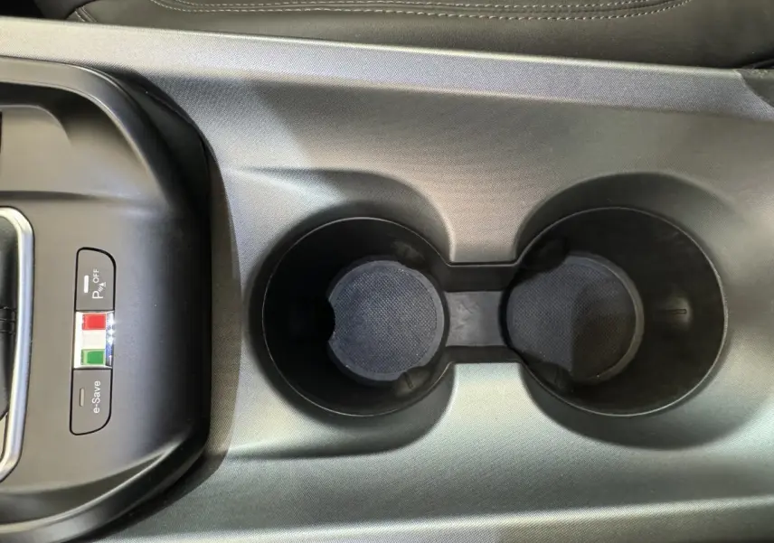 Gros plan sur les porte-gobelets noirs et les boutons de contrôle avec drapeau italien dans la console centrale d'une Alfa Romeo Tonale rouge.