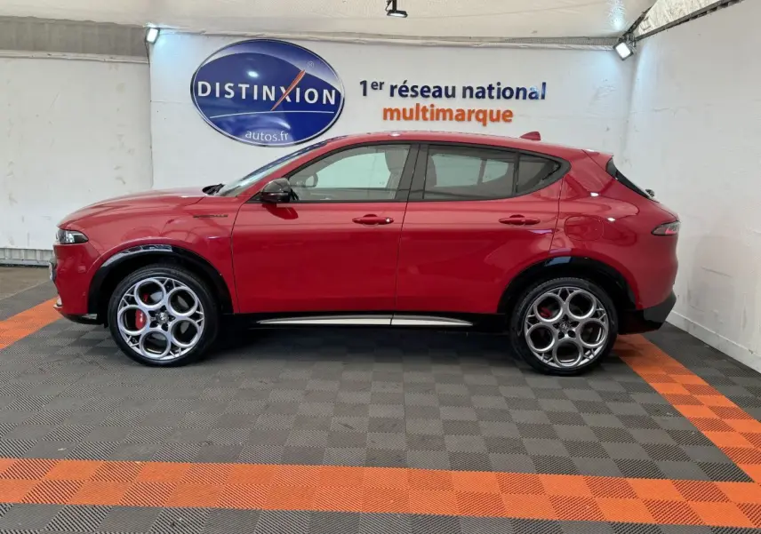 Profil droit d'un Alfa Romeo Tonale rouge 2023 avec jantes originales et détails noirs contrastants dans un showroom.