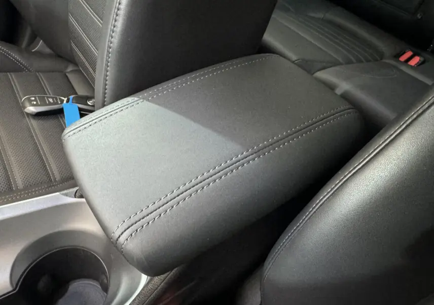 Accoudoir central en tissu noir avec coutures apparentes, siège arrière et clé Alfa Romeo Tonale visible en arrière-plan.