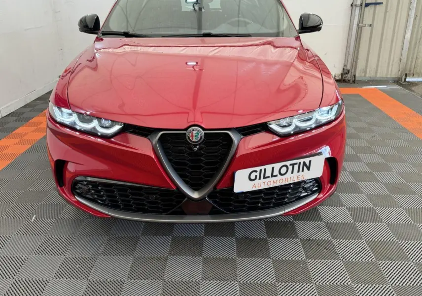 Vue frontale rapprochée de l'Alfa Romeo Tonale rouge avec calandre triangulaire et phares LED allumés.