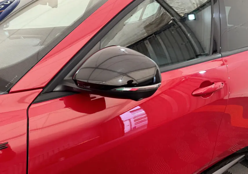 Gros plan sur le rétroviseur noir côté gauche d'une Alfa Romeo Tonale rouge brillante, avec poignée de porte visible.