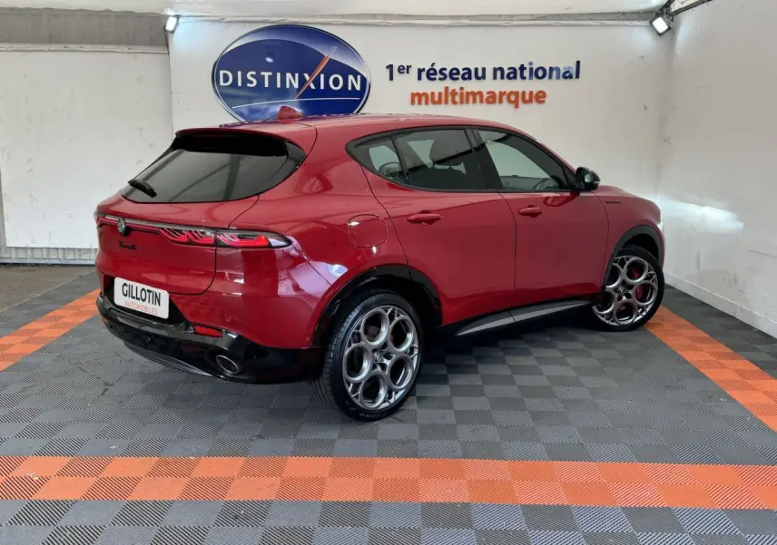 Vue 3/4 arrière droite d'une Alfa Romeo Tonale rouge avec jantes distinctives et feux arrière LED en showroom