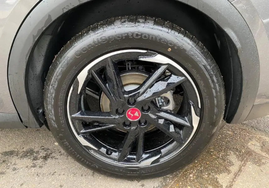 Gros plan sur la jante noire brillante avec logo DS rouge du DS7 Crossback gris platinium, roue avant droite humide.
