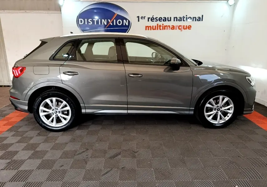 Audi Q3 35 TFSI S Line gris foncé vue de profil côté gauche dans un showroom avec sol à damier noir et rouge.