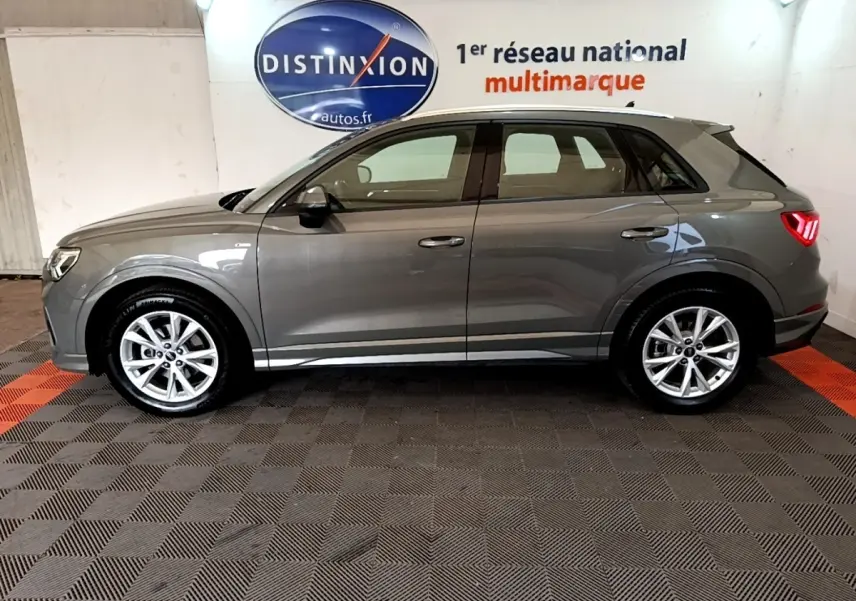 Vue de profil côté gauche d'un Audi Q3 35 TFSI gris foncé avec jantes alliage et feux arrière LED allumés.