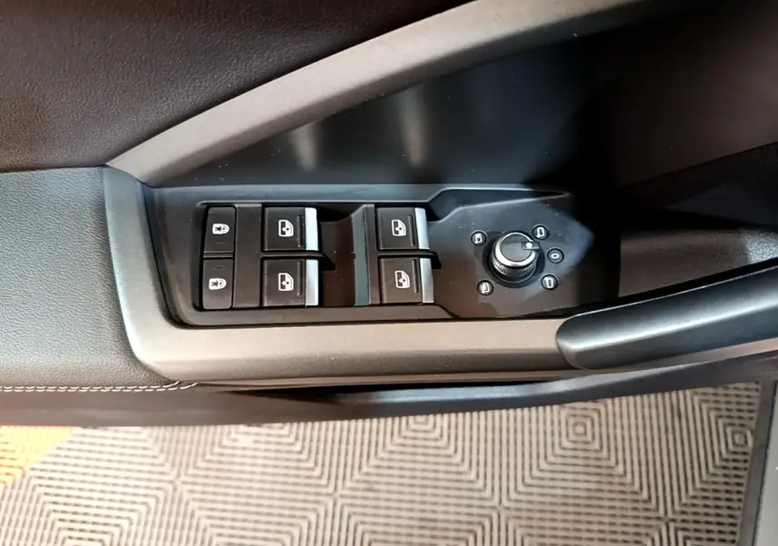 Vue rapprochée des commandes de lève-vitres et réglage des rétroviseurs sur la porte côté conducteur d’un Audi Q3 gris foncé.