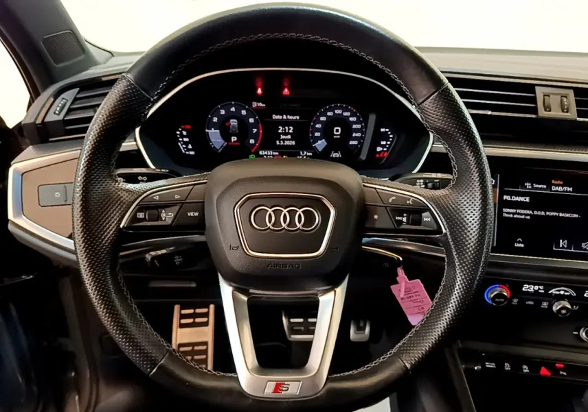 Vue centrée sur le volant cuir multifonctions de l'Audi Q3 gris foncé avec tableau de bord digital et écran tactile.