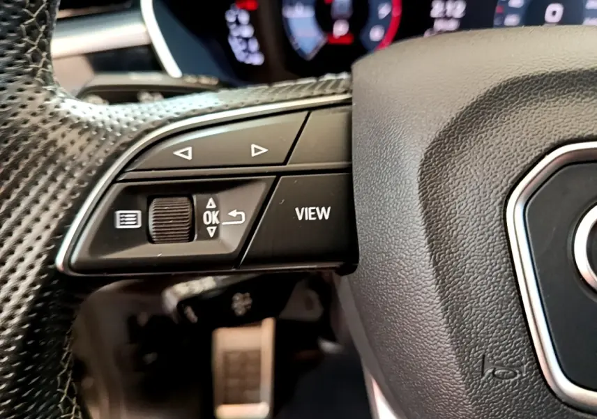 Gros plan sur le volant cuir multifonctions de l'Audi Q3 35 TFSI S Line, boutons de commande et affichage partiel en arrière-plan.