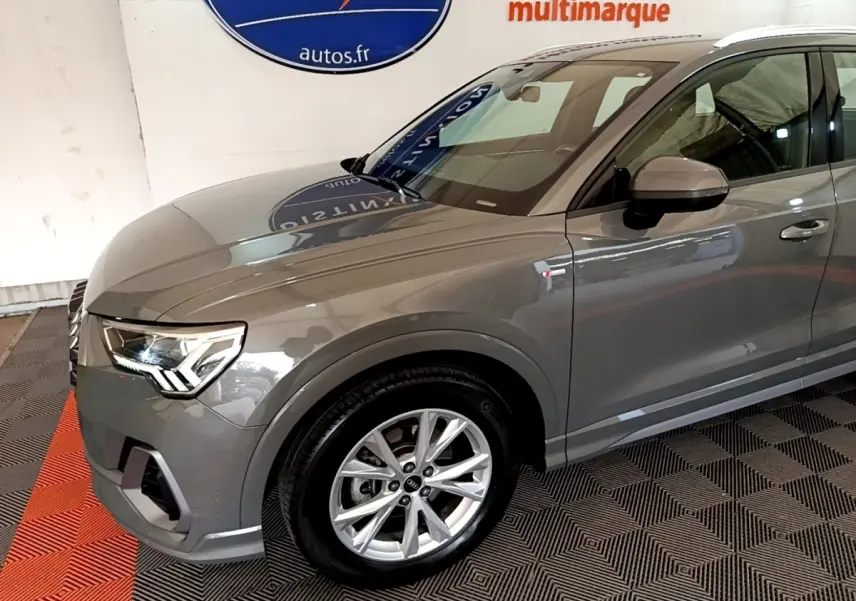 Vue 3/4 avant gauche d'un Audi Q3 gris foncé avec jantes alliage et logo S line sur l'aile avant.
