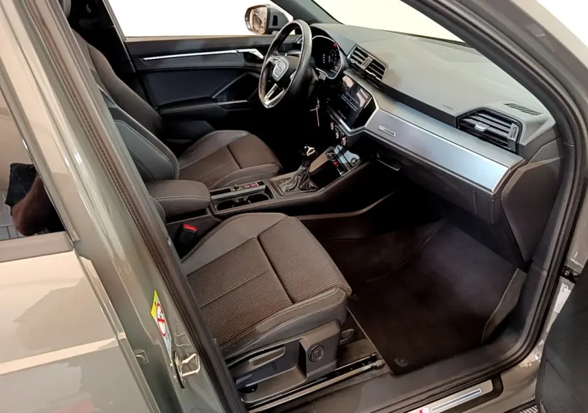 Vue intérieure côté conducteur de l'Audi Q3 gris foncé, mettant en valeur le volant cuir multifonctions et le tableau de bord moderne.