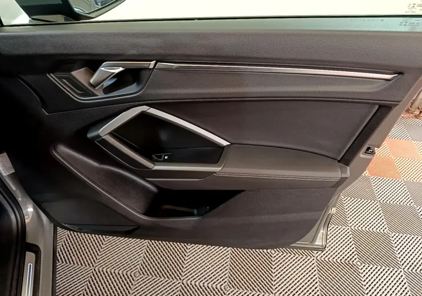 Vue intérieure de la porte avant gauche de l'Audi Q3 gris foncé, avec poignée argentée et garniture noire.