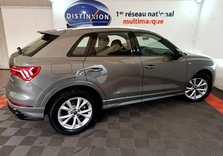 Audi Q3 gris foncé vue de profil côté droit, avec jantes alliage et feux arrière LED allumés.