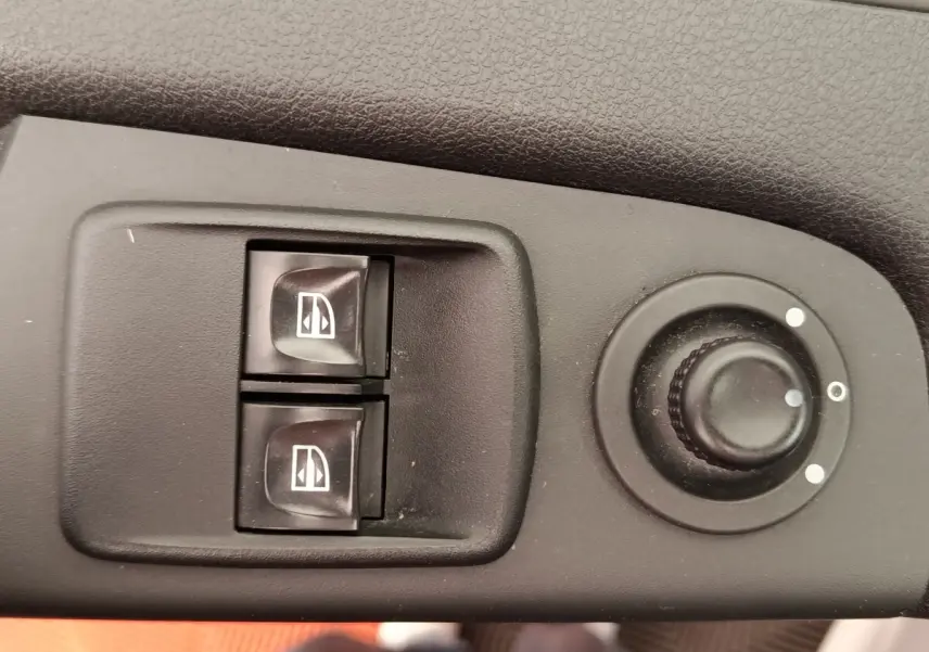 Gros plan sur les commandes électriques des vitres et le réglage des rétroviseurs d’un Renault Trafic Fourgon blanc de 2017.