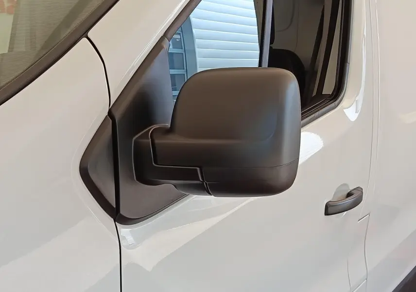 Rétroviseur noir en gros plan sur la porte côté conducteur d’un Renault Trafic fourgon blanc, vue latérale.