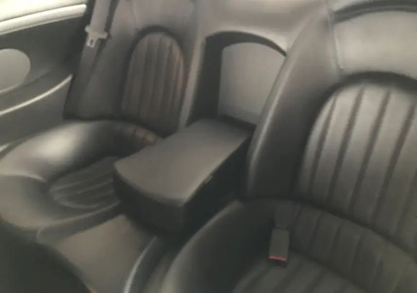 Vue rapprochée des sièges arrière en cuir noir de la Maserati Coupé 2003, soulignant l'accoudoir central.