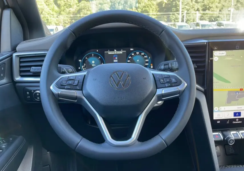 Vue rapprochée du volant multifonction noir du Volkswagen Amarok Simple Cabine 2025 avec tableau de bord numérique et écran tactile.